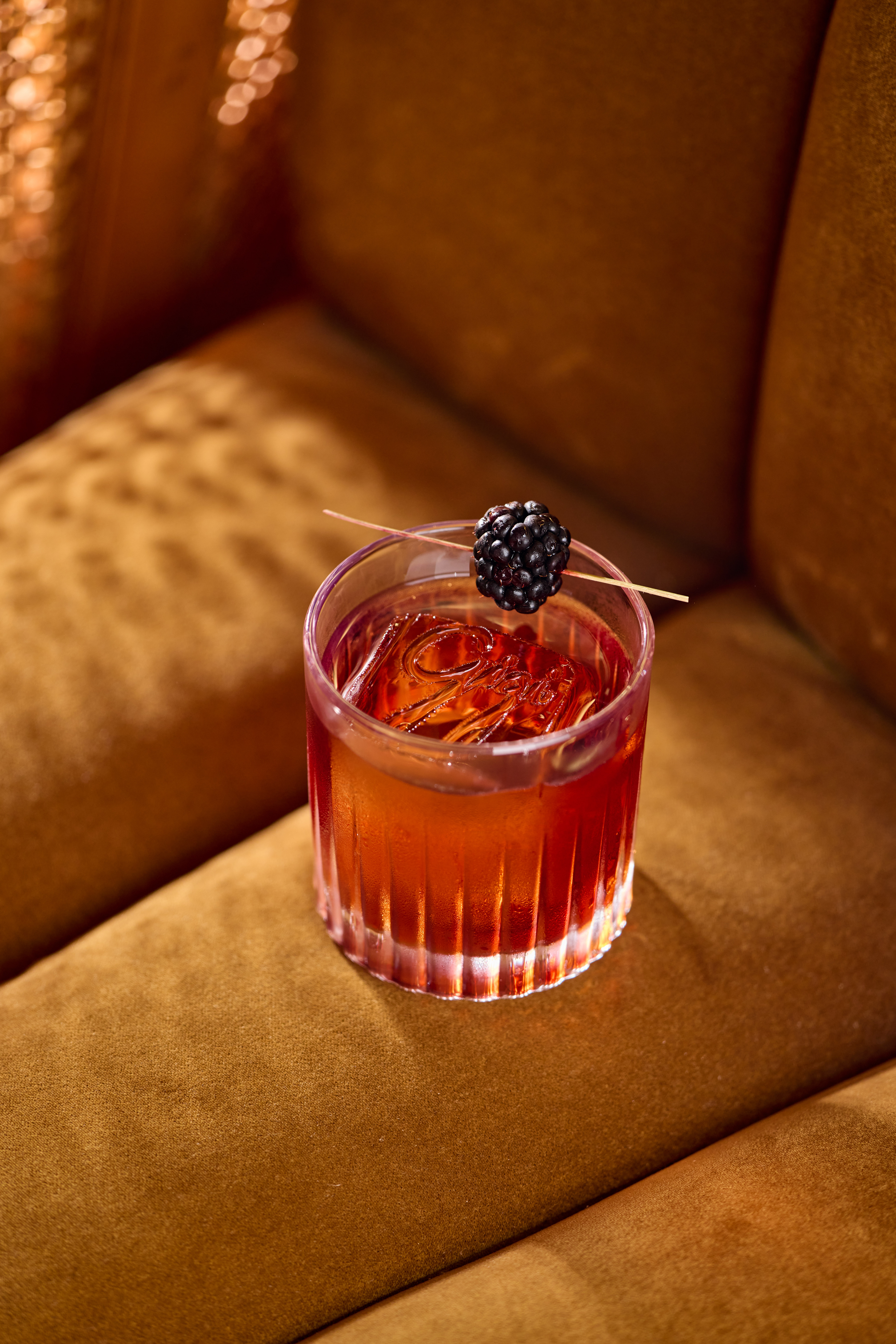 Red cocktail garnished with a blackberry, resting on a mustard-yellow velvet sofa — Delano, Miami