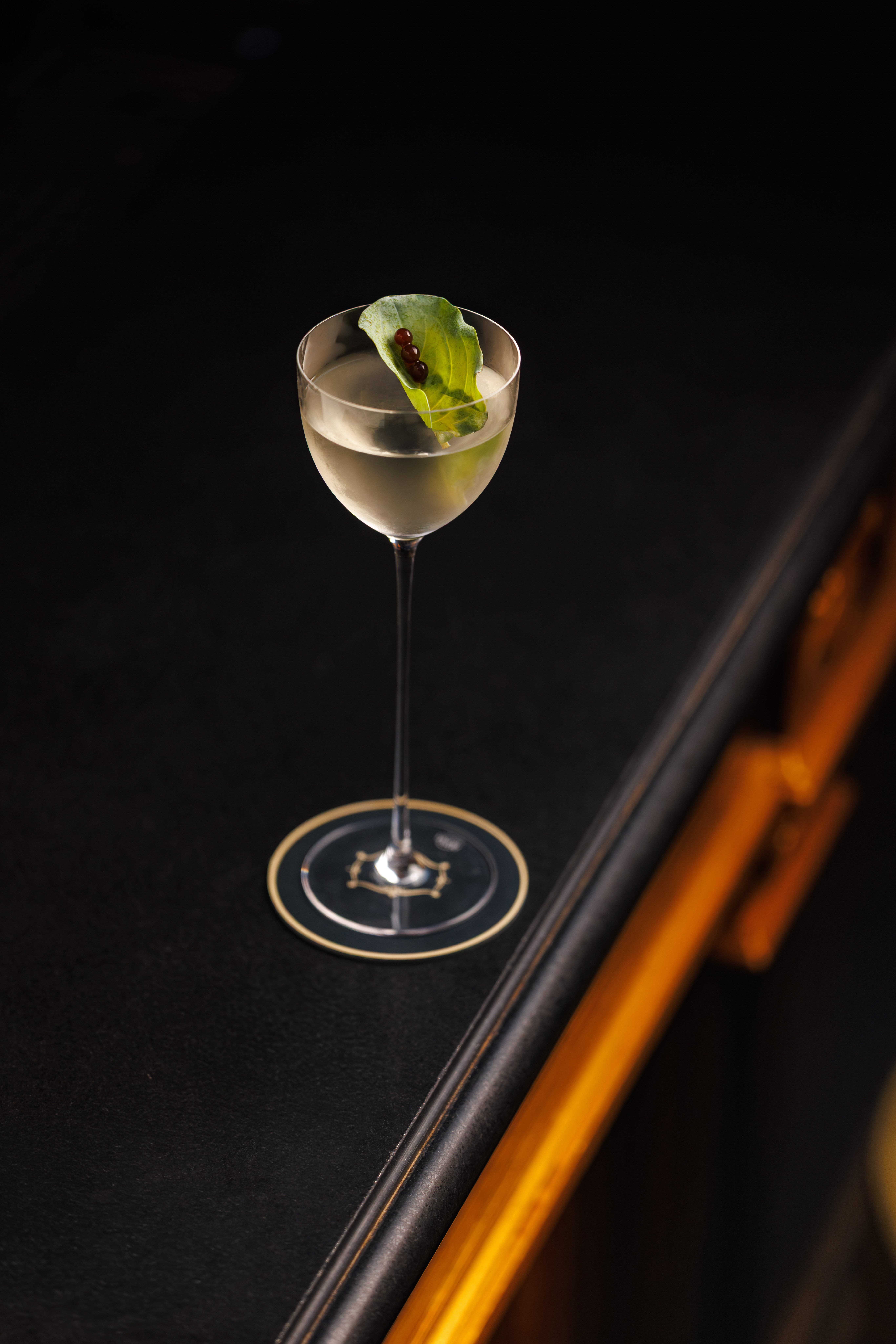 Pale cocktail in a tall stemmed glass spotlit on a dark surface — Four Seasons, Florence