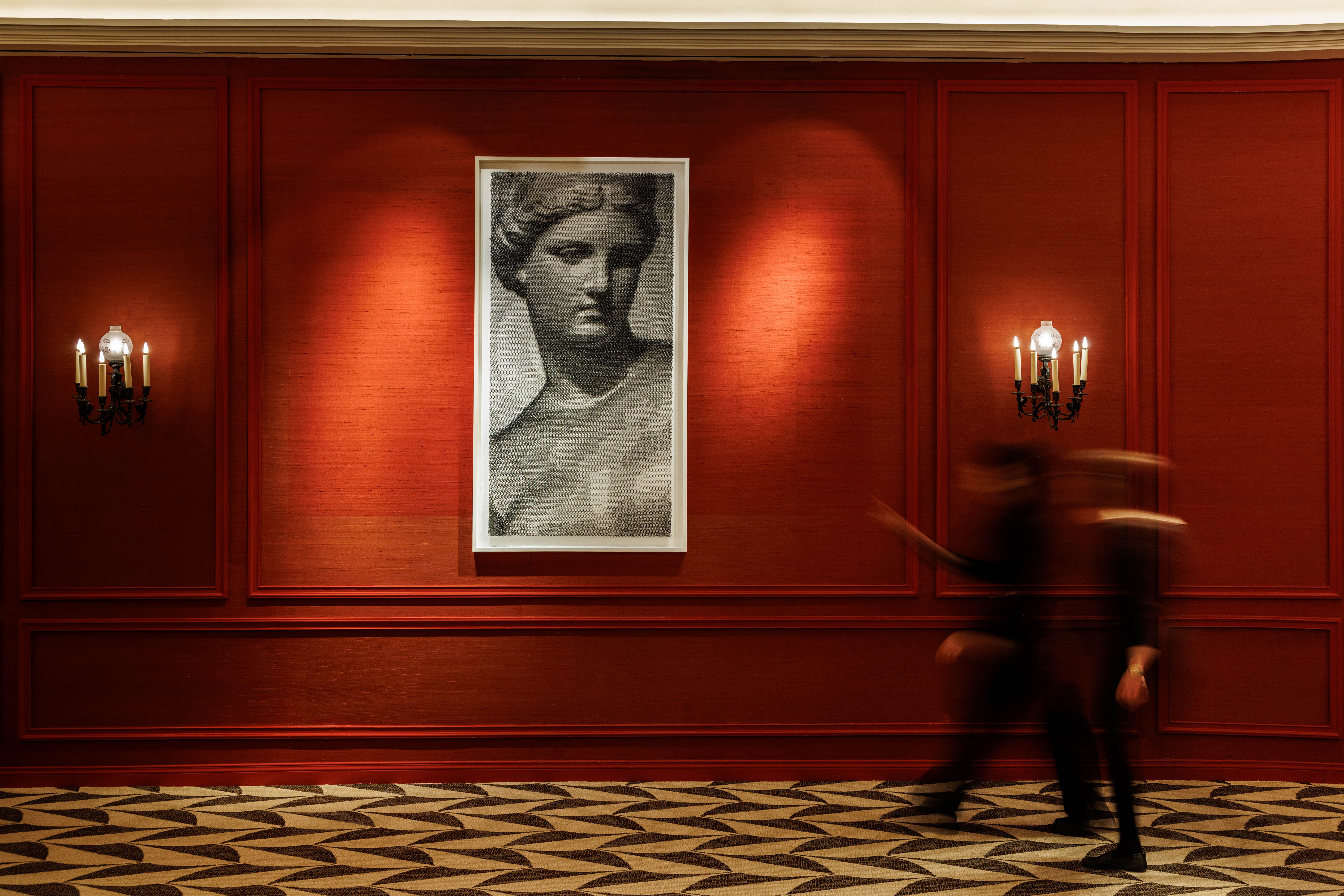 Red-panelled corridor with a framed classical portrait, wall sconces and a patterned carpet