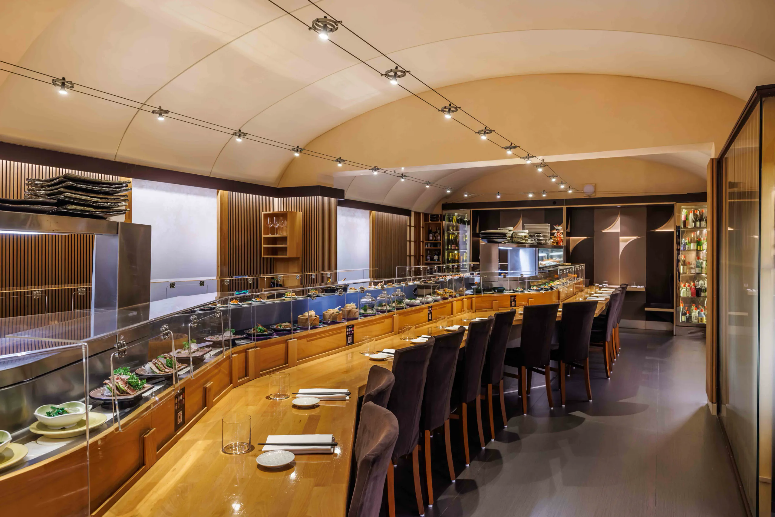 Long illuminated counter with high stools under a curved wooden ceiling