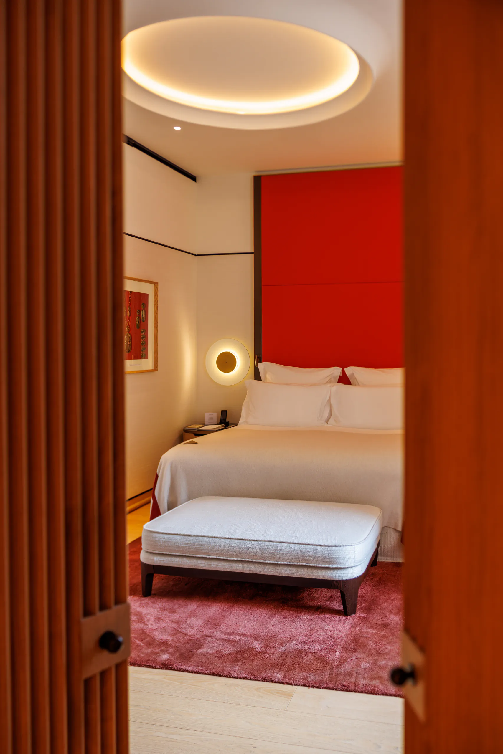 Hotel room seen through a doorway, with a bed and a red accent wall