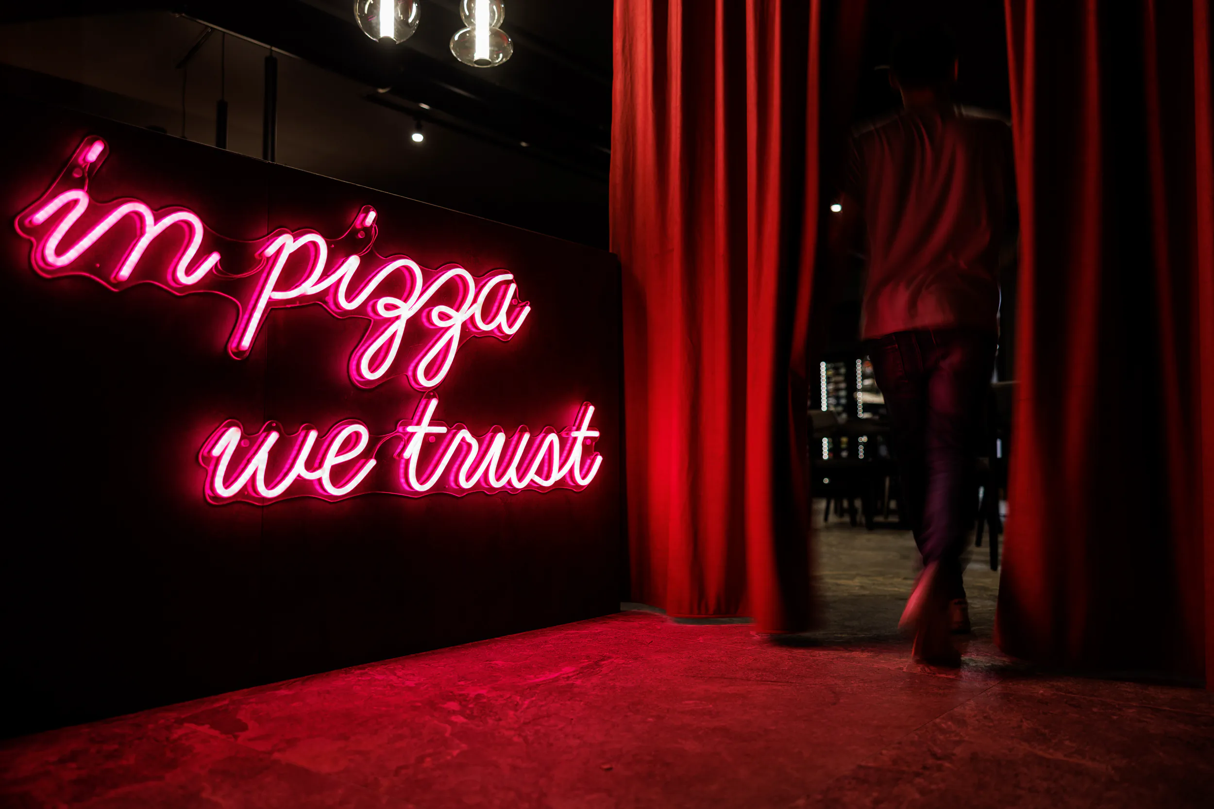 Red room with a neon sign reading 'in pizza we trust'