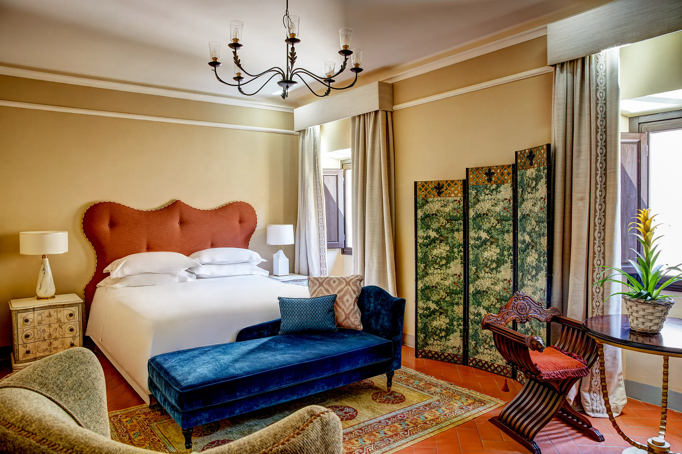 Elegant hotel suite with a red velvet headboard and a blue chaise longue